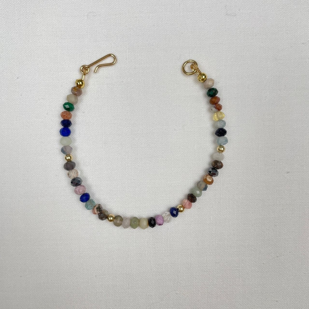 Dit armbandje is geregen van een edelsteen mix afgewisseld met gold filled kraaltjes. De facet kraaltjes zijn 3 x 4 mm en een bonte mix van edelstenen en dus ook van kleuren. Het armbandje sluit met een 14K gold filled haakje.