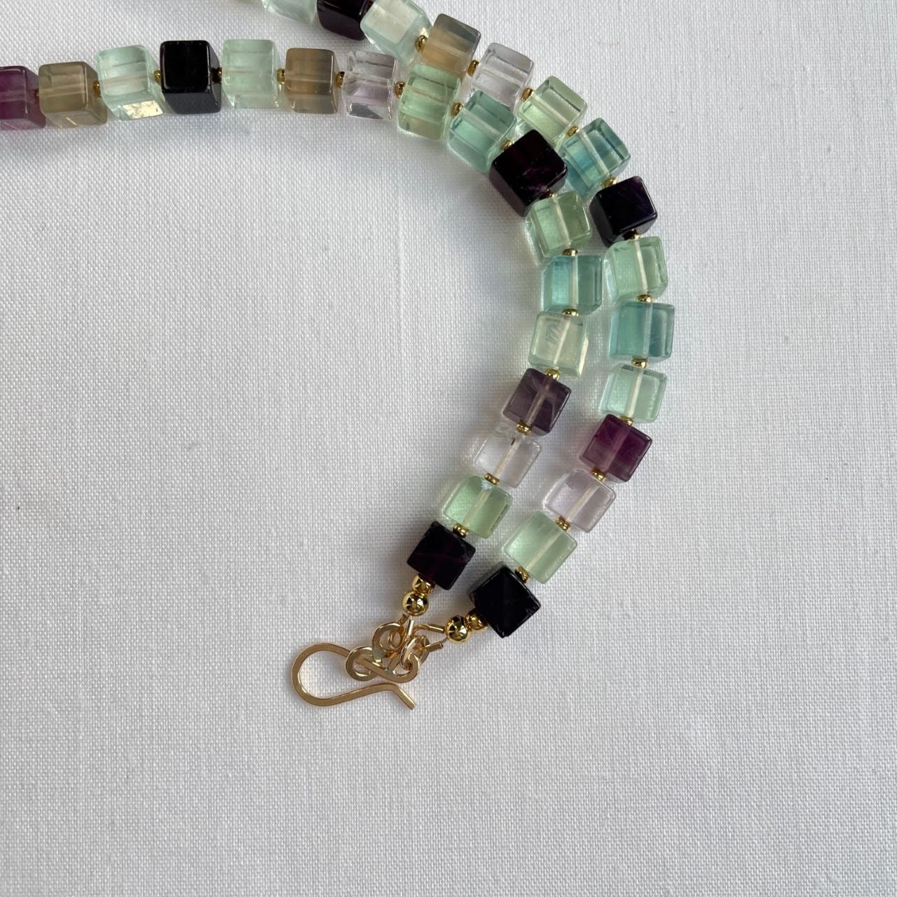 Ketting van transparante fluoriet cubes in diverse kleuren, afgewisseld met 24K gold plated kraaltjes. De kleuren gaan van lichtroze naar groen, naar paars. Fluoriet heeft een beschermende werking, die het zelfvertrouwen vergroot. De choker sluit met een 14K gold filled slot in de vorm van een haakje.