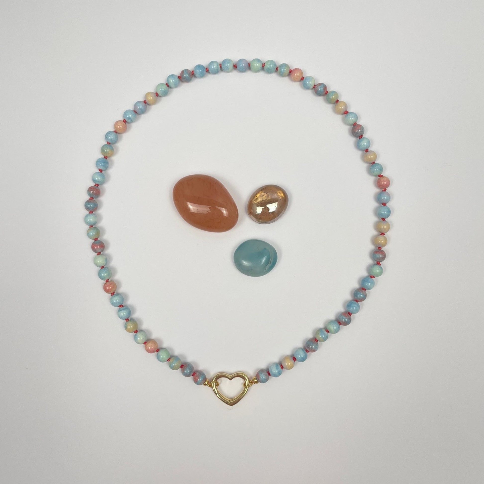 De ketting is geknoopt met koraalkleurige zijde van 6 mm kralen Mongoolse agaat. Deze kralen hebben veel verschillende lichte kleurtjes; blauw, groen, geel en oranje. De ketting eindigt met twee ringetjes waar een sluiting tussen kan worden gemaakt. Hier is dat een 18K gold filled hartje