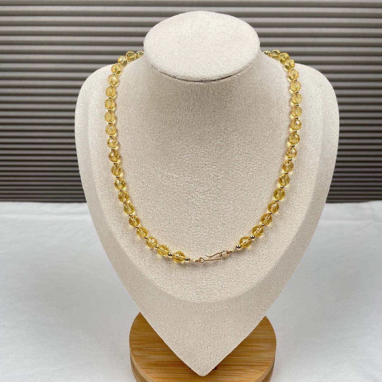 Ketting geregen van citrien facetkralen met heel veel facetjes en daartussen kleine gold filled kraaltjes. Afgewerkt met een paar grotere gold filled kraaltjes en een slotje in de vorm van een haakje. De ketting hangt op een display.