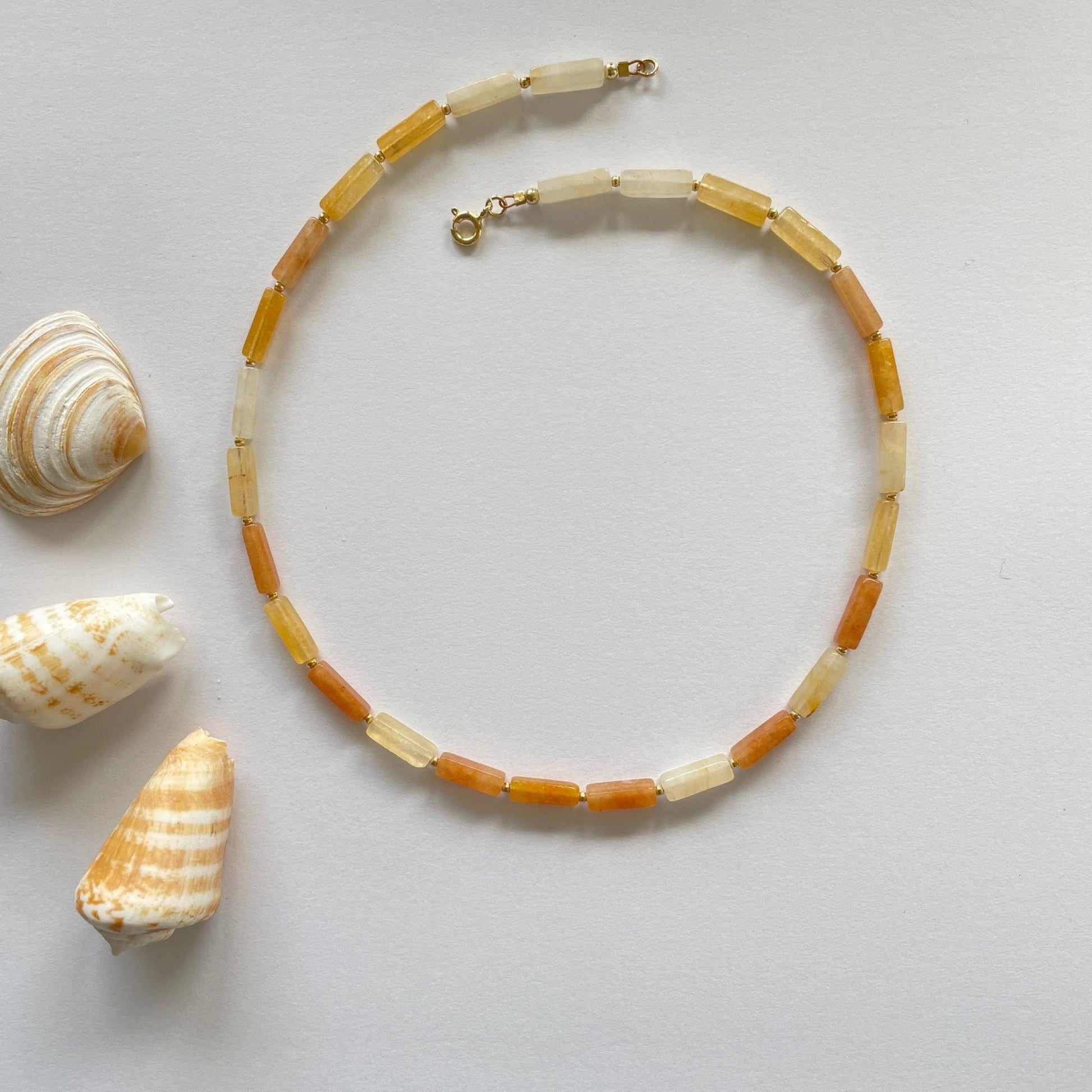 Ketting van gele aventurijn staafje met kleine gold filled kraaltjes en een een gold filled veerslotje. Naats de ketting liggen drie schelpen in dezelfde tinten. 