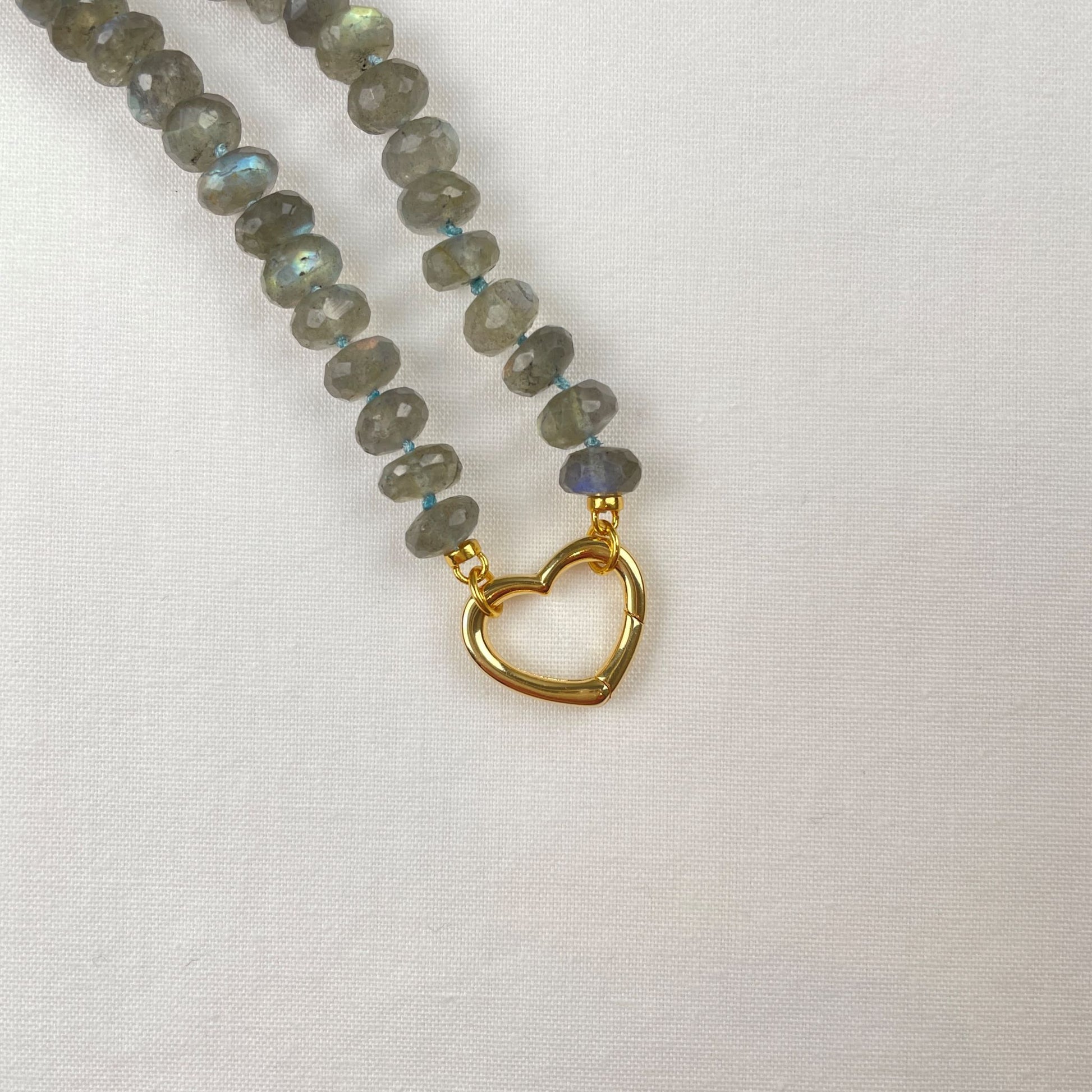 Ketting van facetgeslepen labradoriet rondel kralen. De ketting is geknoopt met blauwe zijde en sluit met een 18K gold filled hartvormig slot.